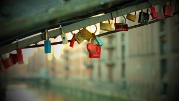 Mehrere bunte Liebesschlösser an einer Brücke, symbolisieren ewige Liebe und Verbundenheit, mit urbanem Hintergrund.