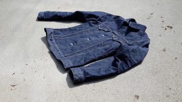 Michael Stevens trägt eine dunkle Jeansjacke, liegt auf einem Betonboden, wirkt entspannt und stilvoll. Perfekt für Mode- und Lifestyle-Inhalte.