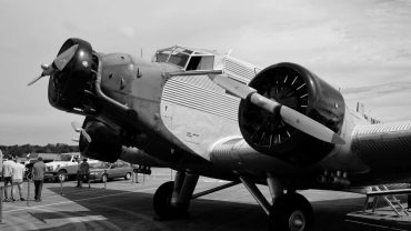 Historisches Flugzeug auf einer Flugschau, mit Besuchern im Hintergrund, in Schwarz-Weiß aufgenommen.