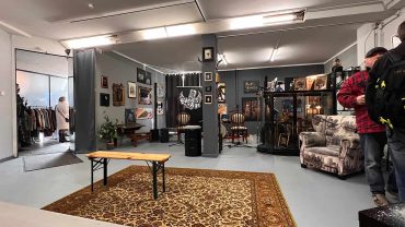 Kunst- und Antiquitätenladen mit Michael Stevens, der vor Gemälden und Skulpturen steht, umgeben von Vintage-Möbeln und Kunstwerken.
