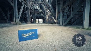 Michael Stevens steht unter einer großen Brücke mit Stahlträgern, im Vordergrund liegt eine Blundstone-Schuhbox auf dem Boden.