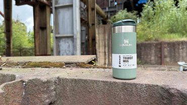 Stanley Transit Mug auf einer Steinmauer im Freien, ideal für unterwegs, langlebig und isolierend.