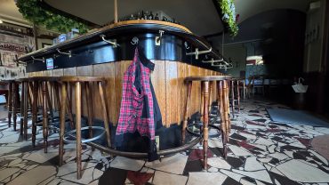 Bar mit Hockern und Jacke im Vordergrund, leere Innenraum mit stilvollem Design, ideal für entspannte Abende.