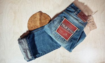 Hochwertige Jeans mit Label und Hut auf Holzuntergrund, ideal für modebewusste Männer. Perfekt für Casual- und Streetwear-Looks, zeigt Stil und Komfort.