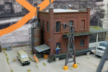 Modell eines Industriegebäudes mit Figuren, Fahrzeugen und elektrischen Anlagen, detailreiche Miniaturdarstellung eines industriellen Szenarios.