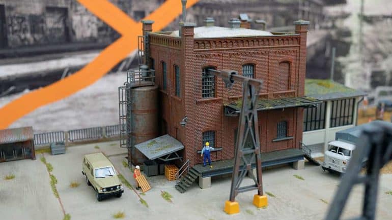 Modell eines Industriegebäudes mit Figuren, Fahrzeugen und elektrischen Anlagen, detailreiche Miniaturdarstellung eines industriellen Szenarios.